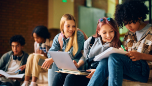 Happy teenager using a laptop while studying with her classmates in High Scholl